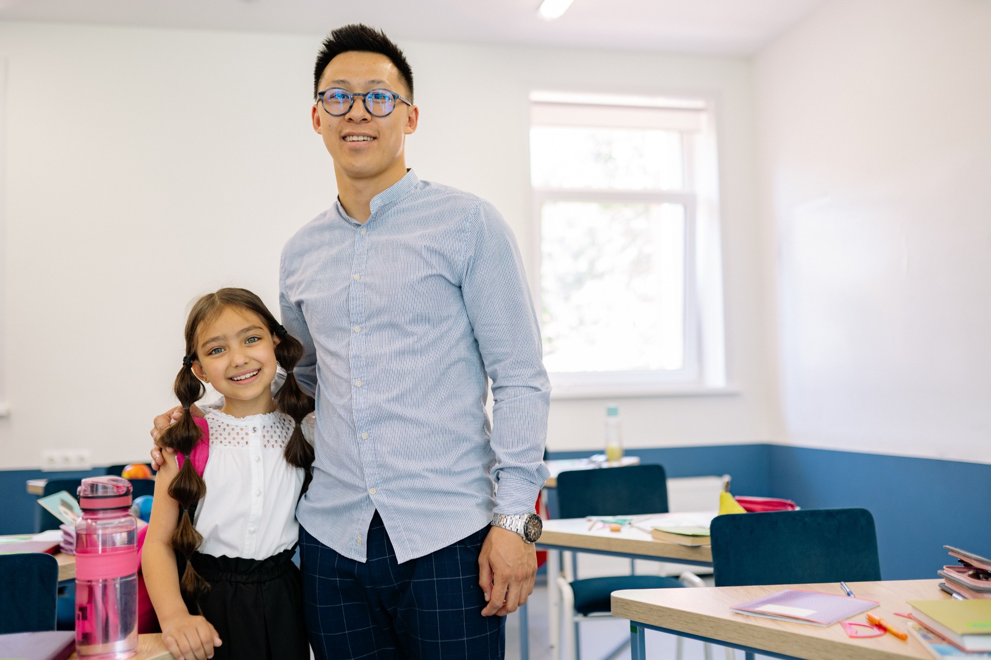 A teacher and young student smile together in a bright classroom